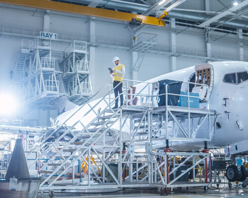 Engineer in Safety Vest Standing next to Airplane in Hangar