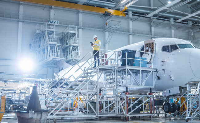 Engineer in Safety Vest Standing next to Airplane in Hangar